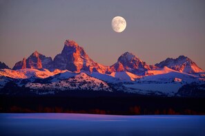 Un paysage de montagne avec des sommets enneigés et une pleine lune dans le ciel.