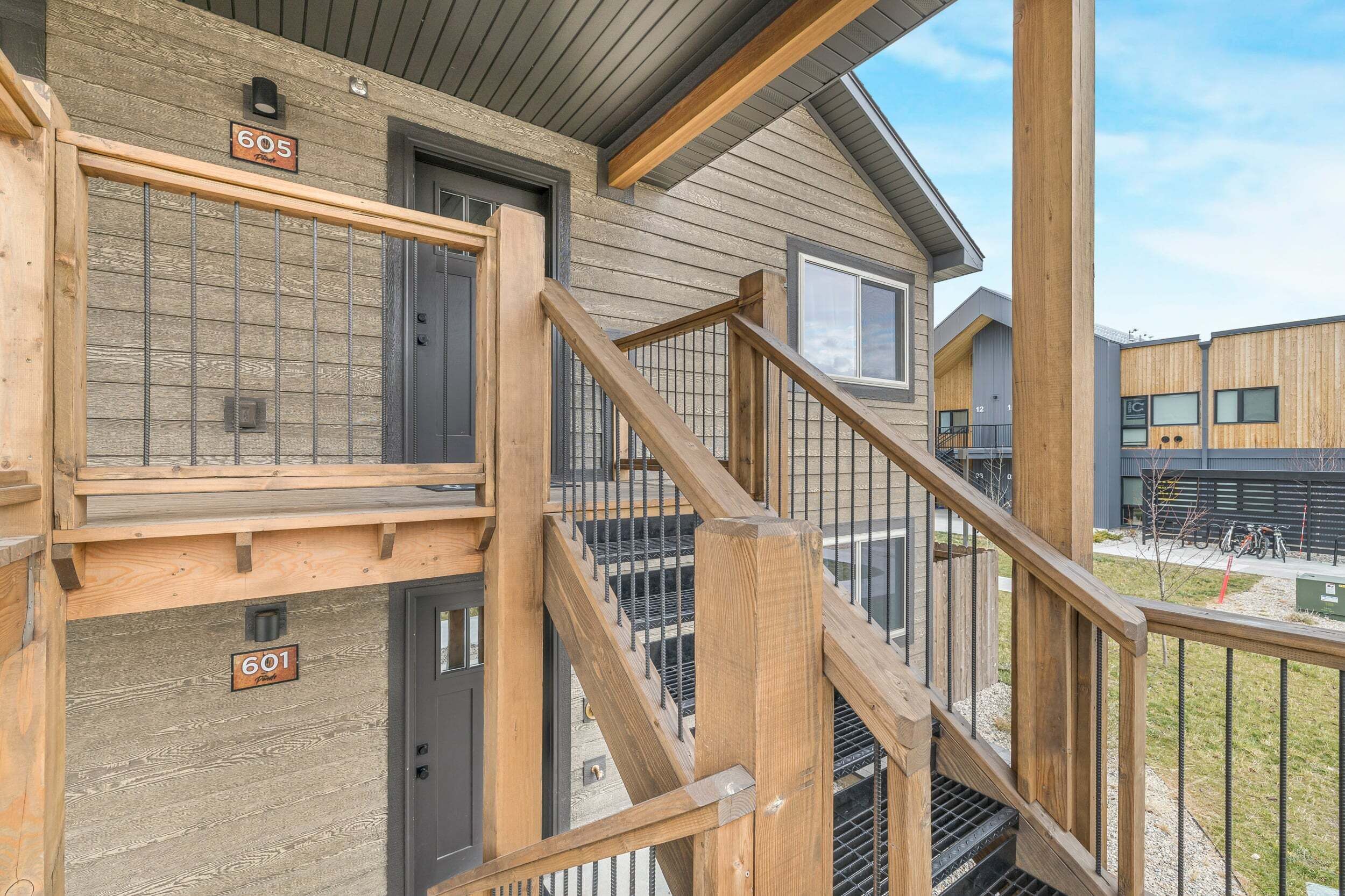 A multi-story building with wooden railings and metal grates, featuring numbered doors and a visible staircase.