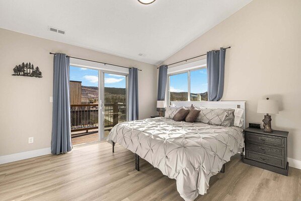A bedroom with a bed, a nightstand, a window, and a view of the outdoors.
