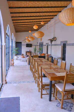 A long dining table with chairs, a television, and potted plants in a room with a high ceiling and large windows. - Villa Marine Privée (heated pool, 5 bdrms) (Marrakech)
