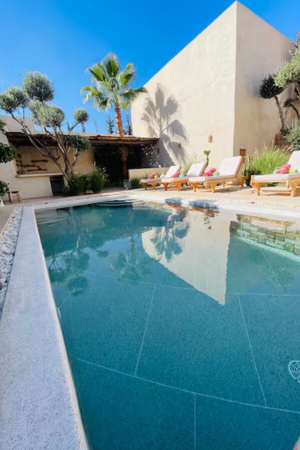 A swimming pool with lounge chairs, palm trees, and a building with a geometric facade. - Villa Marine Privée (heated pool, 5 bedrooms) (Marrakech)