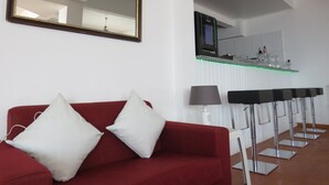 Ein modernes Hotelzimmer mit einem roten Sofa, einem großen Spiegel, einem Fernseher und einer Bar mit einer grün beleuchteten Theke.
