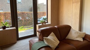 A modern living room with a brown leather sofa, a wooden cabinet, and a large sliding glass door leading to a garden.