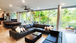 A modern living room with a sectional sofa, a dining area, and large windows with a view of greenery. - Luxurious Villa in Amapas, Zona Romantica, Malecon! (Puerto Vallarta)