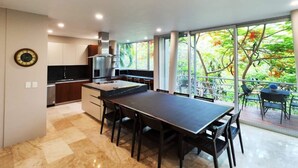 A modern kitchen with a dining area, large windows, and a view of trees. - Luxurious Villa in Amapas, Zona Romantica, Malecon! (Puerto Vallarta)