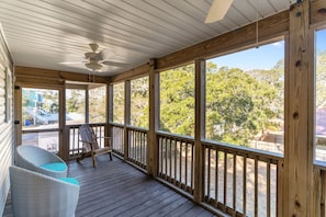 A covered porch with a ceiling fan, wooden railings, and wicker chairs.