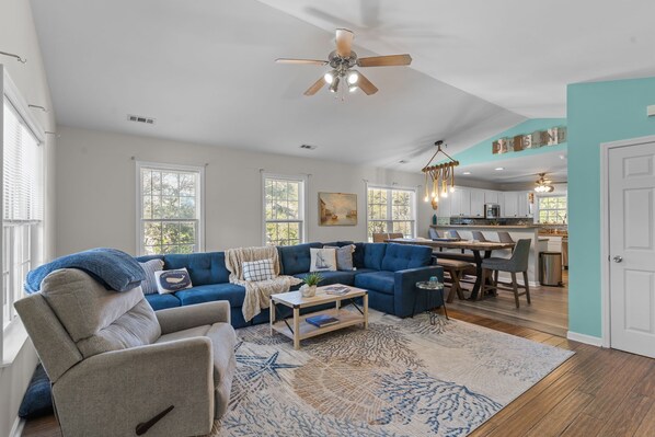 A spacious living room with a sectional sofa, a coffee table, and a dining area with a kitchen in the background.