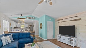 Een moderne woonkamer met een blauwe modulaire bank, een houten salontafel, een televisie op een witte kast en een plafondventilator.