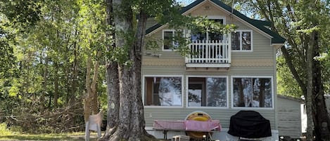 A two-story house with a balcony, large windows, and a covered outdoor seating area.