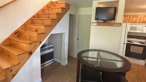 A staircase with wooden steps leading to a landing, a kitchen area with a microwave and oven, and a glass-top table with two chairs. - Serene 2-bedroom lake house in welcoming Unity, perfect for relaxing stays (Unity)