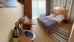 A hotel room with a bed, a desk with a chair, a coffee maker, and a plant. - Willa Balticus Władysławowo (Władysławowo)