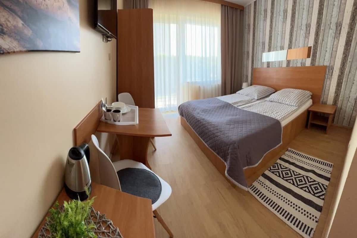 A hotel room with a bed, a desk with a chair, a coffee maker, and a plant.