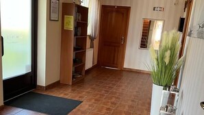 A hallway with a tiled floor, a door, a bookshelf, and a potted plant. - Willa Balticus Władysławowo (Władysławowo)