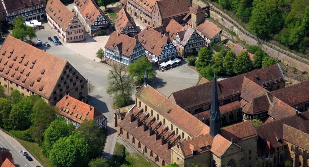 An aerial view of a historic town with traditional half-timbered buildings, a central square, and a church with a prominent steeple.