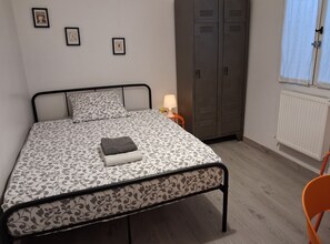 A single bed with a patterned bedspread, a bedside lamp, a wardrobe, and a chair. - First floor room in a town house. (La Riche)