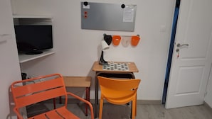 A room with a television, a desk with a lamp, two chairs, a board with buttons, and a door. - First floor room in a town house. (La Riche)
