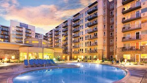 Ein mehrstöckiges Hotel mit Schwimmbad, Sitzgelegenheiten im Freien und Balkonen.