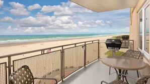 Ein Balkon mit Blick auf den Strand, einem Grill und einem Tisch mit Stühlen.