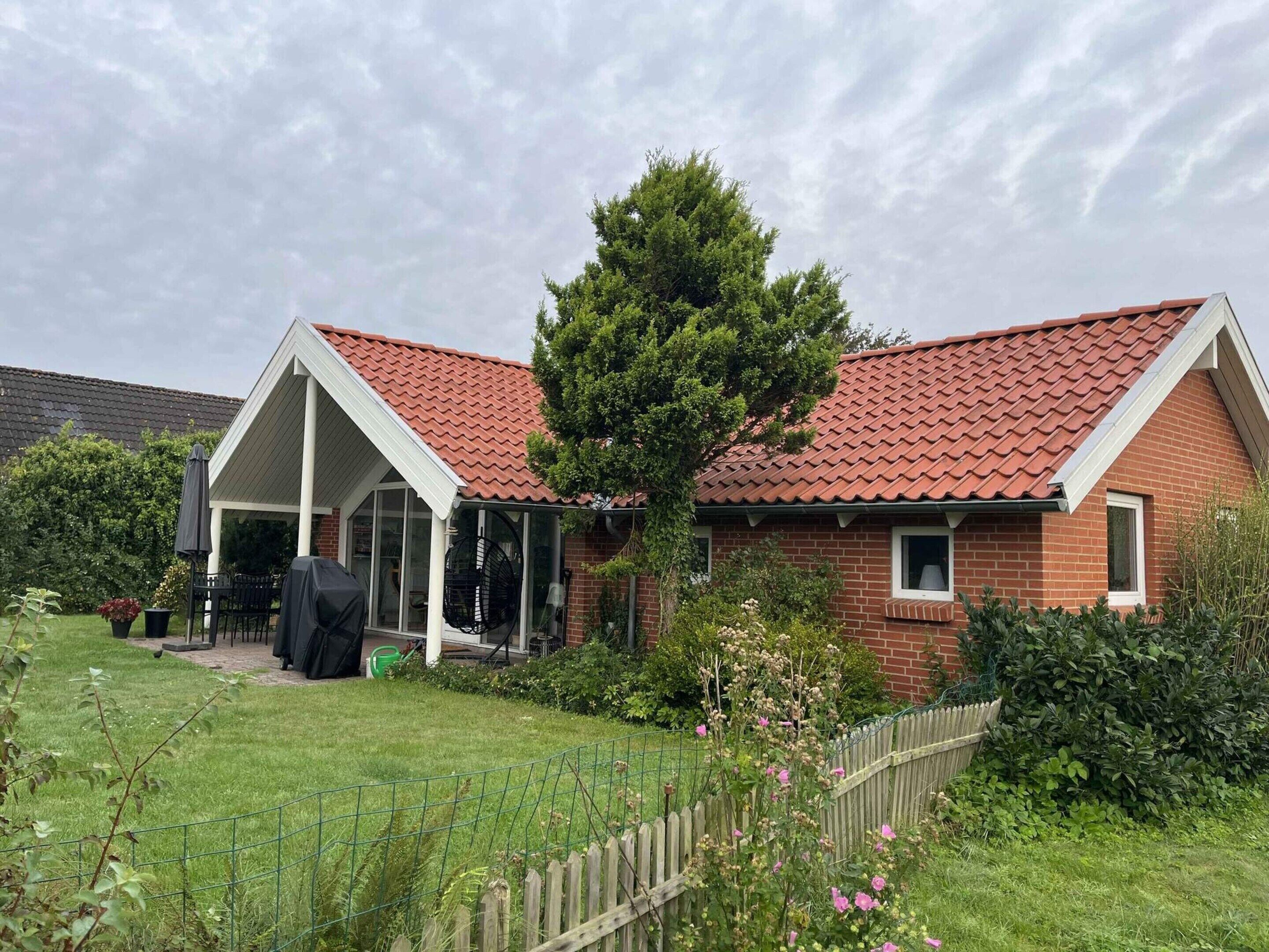 A brick house with a red-tiled roof, a covered porch, and a fenced yard.