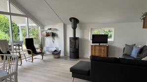 En stue med en sort sofa, et fjernsyn, en pejs og et spiseområde med stole og et bord.