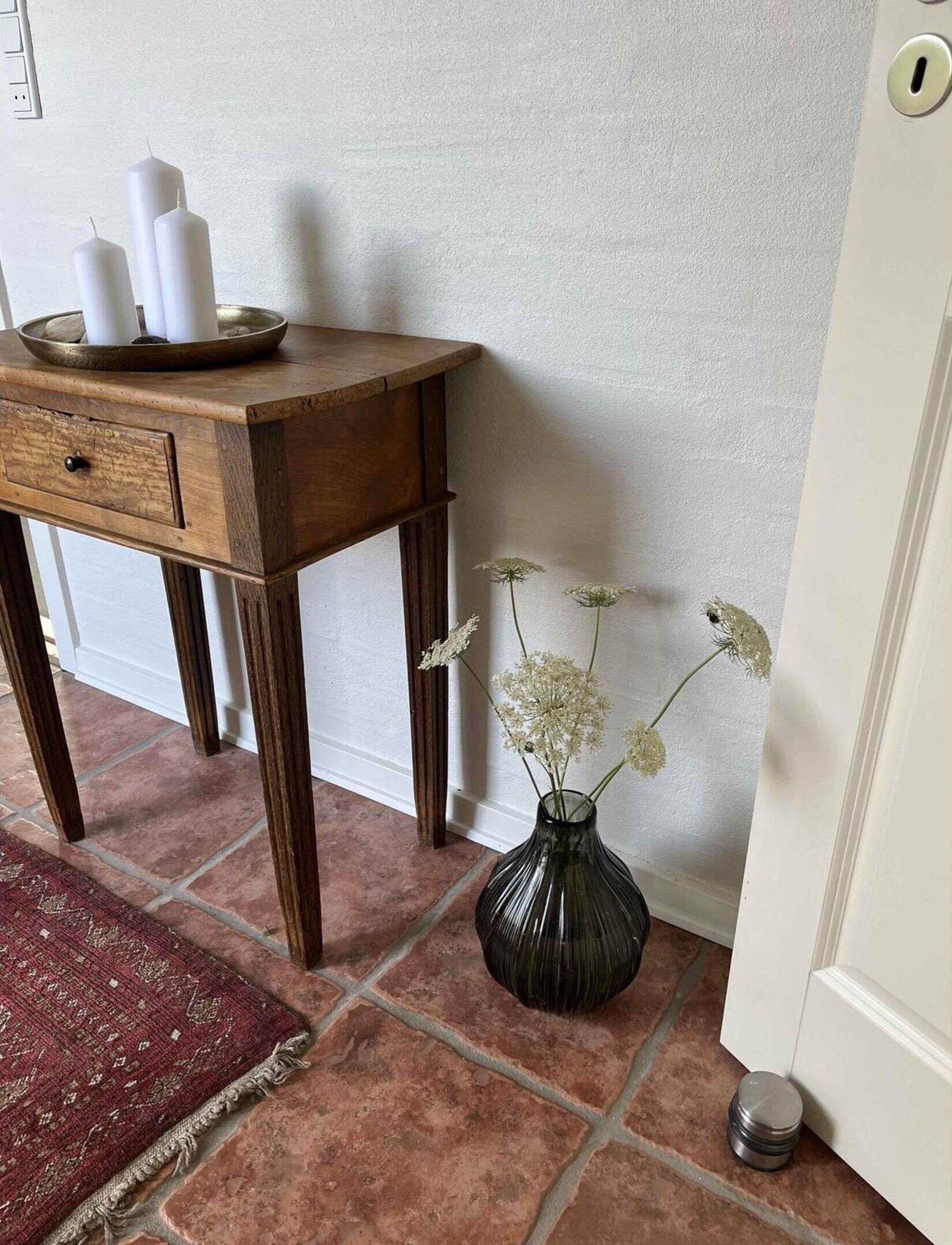 Una mesita de madera con velas, un florero con flores y una alfombra sobre un suelo de baldosas.