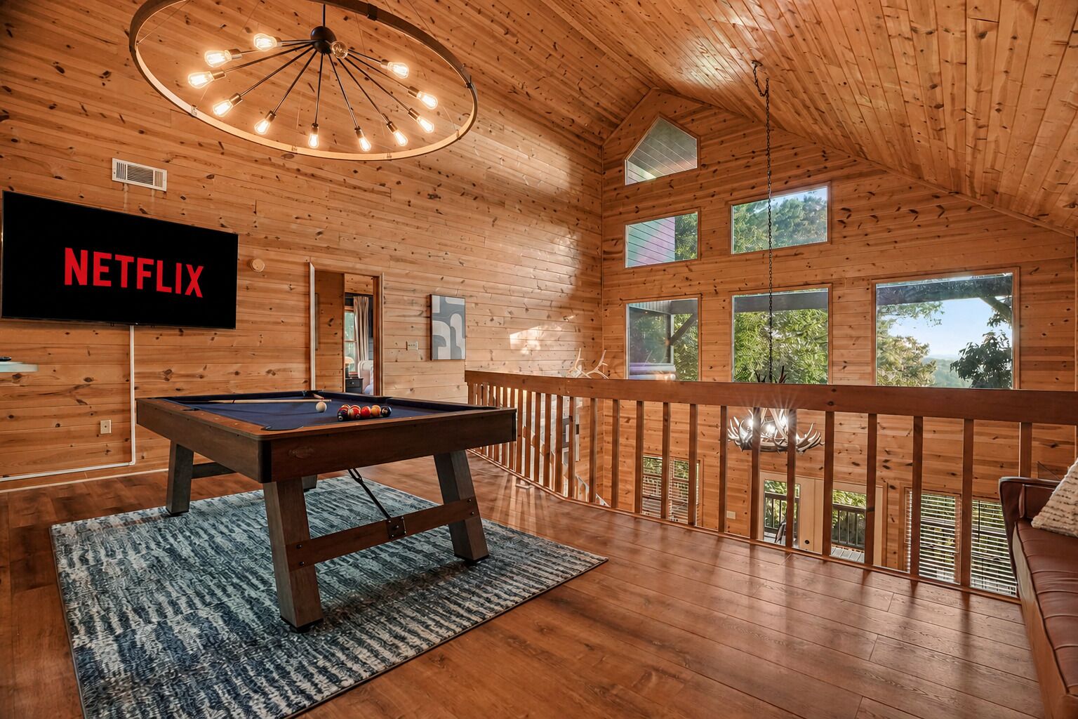 A wooden interior with a pool table, a TV screen displaying 'NETFLIX,' and a balcony with a view.