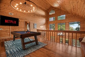 Ein Holzinterieur mit Billardtisch, einem Fernseher, der 'NETFLIX' anzeigt, und einem Balkon mit Aussicht.