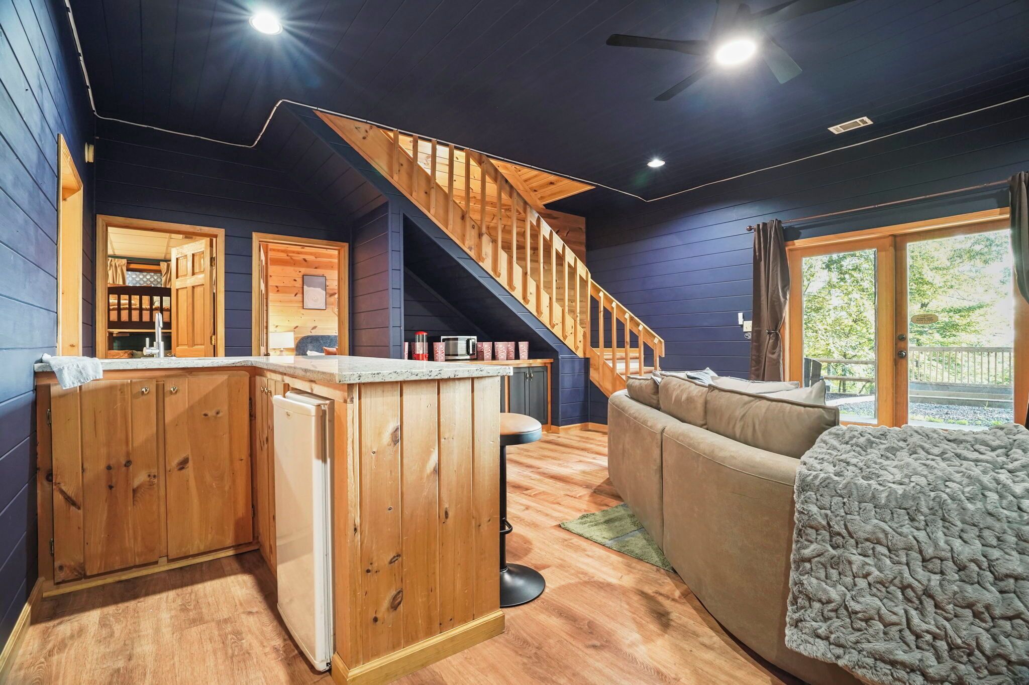 A modern cabin interior with a kitchen, dining area, and a wooden staircase.