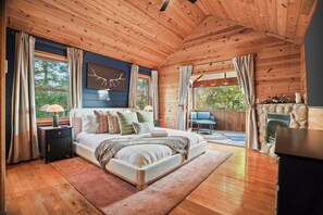 A spacious bedroom with a large bed, a nightstand, a dresser, and a stone fireplace. - Pine & Peak - Views - 2 Masters - Hottub - Stargazing Net - Movie Room - Playset (Morganton)