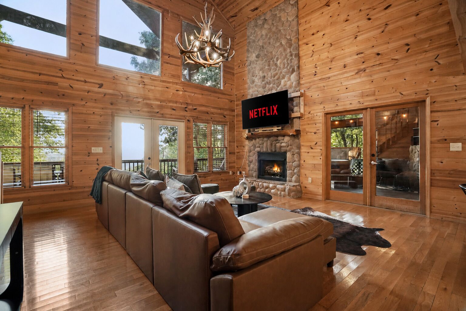 A log cabin interior with a stone fireplace, leather sofa, and a Netflix TV mounted on the wall.