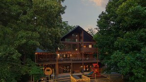 Eine zweistöckige Holzhütte mit einer Terrasse, Sitzgelegenheiten im Freien und einem Spielbereich.