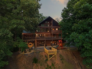 A two-story log cabin with a deck, outdoor seating, and a play area. - Pine & Peak - Views - 2 Masters - Hottub - Stargazing Net - Movie Room - Playset (Morganton)