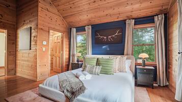 A wooden cabin bedroom with a bed, nightstands, a window with curtains, and a wall-mounted artwork.