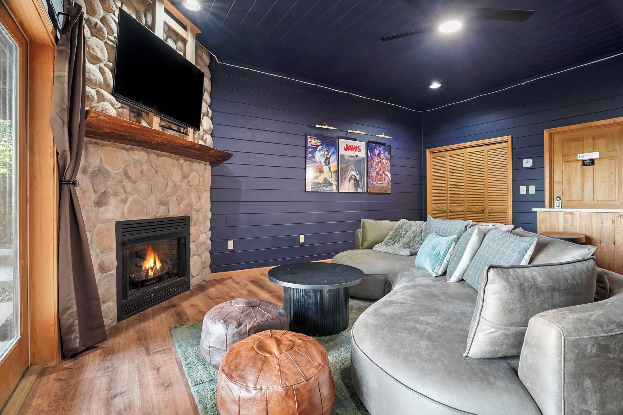A cozy living room with a stone fireplace, a large gray sofa, and a flat-screen TV mounted on the wall.
