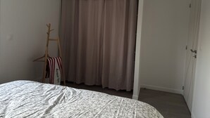 Ein Schlafzimmer mit Bett, Kleiderschrank, Kleiderhaken und Vorhang.