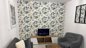 Ein Wohnzimmer mit grauem Sofa, grauem Sessel, Couchtisch aus Holz und einem Fernseher auf einem Holzschrank.