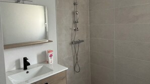 Ein Badezimmer mit einem weißen Waschbecken, einem Spiegel, einer Dusche inklusive Duschhandstück und einem Seifenspender.