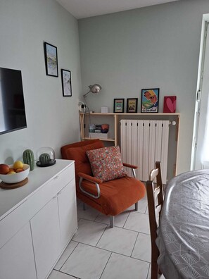 A compact living space with a white cabinet, a red chair with a patterned cushion, a dining table with a patterned tablecloth, and a radiator. - Apartment Veronica - your cocoon with terrace in the center of La Bourboule (La Bourboule)