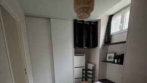 Et soveværelse med seng, garderobeskab, stol, hylde med genstande og et vindue.