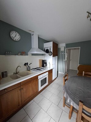 A kitchen with a stove, sink, and cabinets, a dining table with chairs, and a clock on the wall. - Apartment Veronica - your cocoon with terrace in the center of La Bourboule (La Bourboule)
