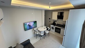 Una sala de estar moderna con sofá, televisor, mesa de comedor con sillas, lavadora y área de cocina.