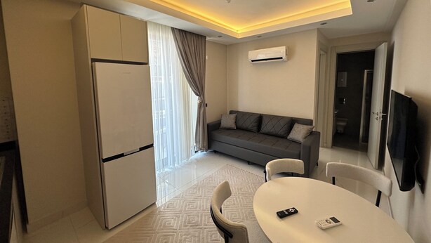 Una habitación de hotel moderna con kitchenette, un sofá, una mesa de comedor y un televisor.