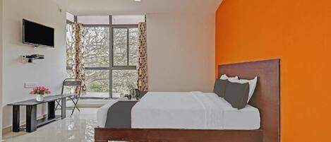 Une chambre à coucher avec un lit, une télévision, un bureau et une fenêtre avec des rideaux.