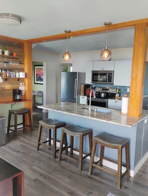 Une cuisine moderne dotée d’un îlot central, de tabourets de bar, de poutres en bois et de luminaires suspendus.