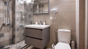 A modern bathroom with a glass-enclosed shower, a vanity with a sink, a toilet, and a hairdryer mounted on the wall. - Carmen Sea View Maisonette (Lefkada)