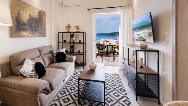 A living room with a sofa, coffee table, TV, and a view of the sea. - Carmen Sea View Maisonette (Lefkada)