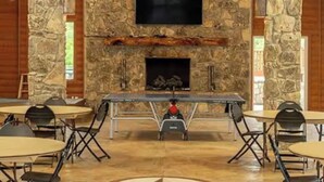 A stone fireplace with a flat-screen TV above it, surrounded by tables and chairs. - NEW! Resort and Cozy Cottage (Austin)