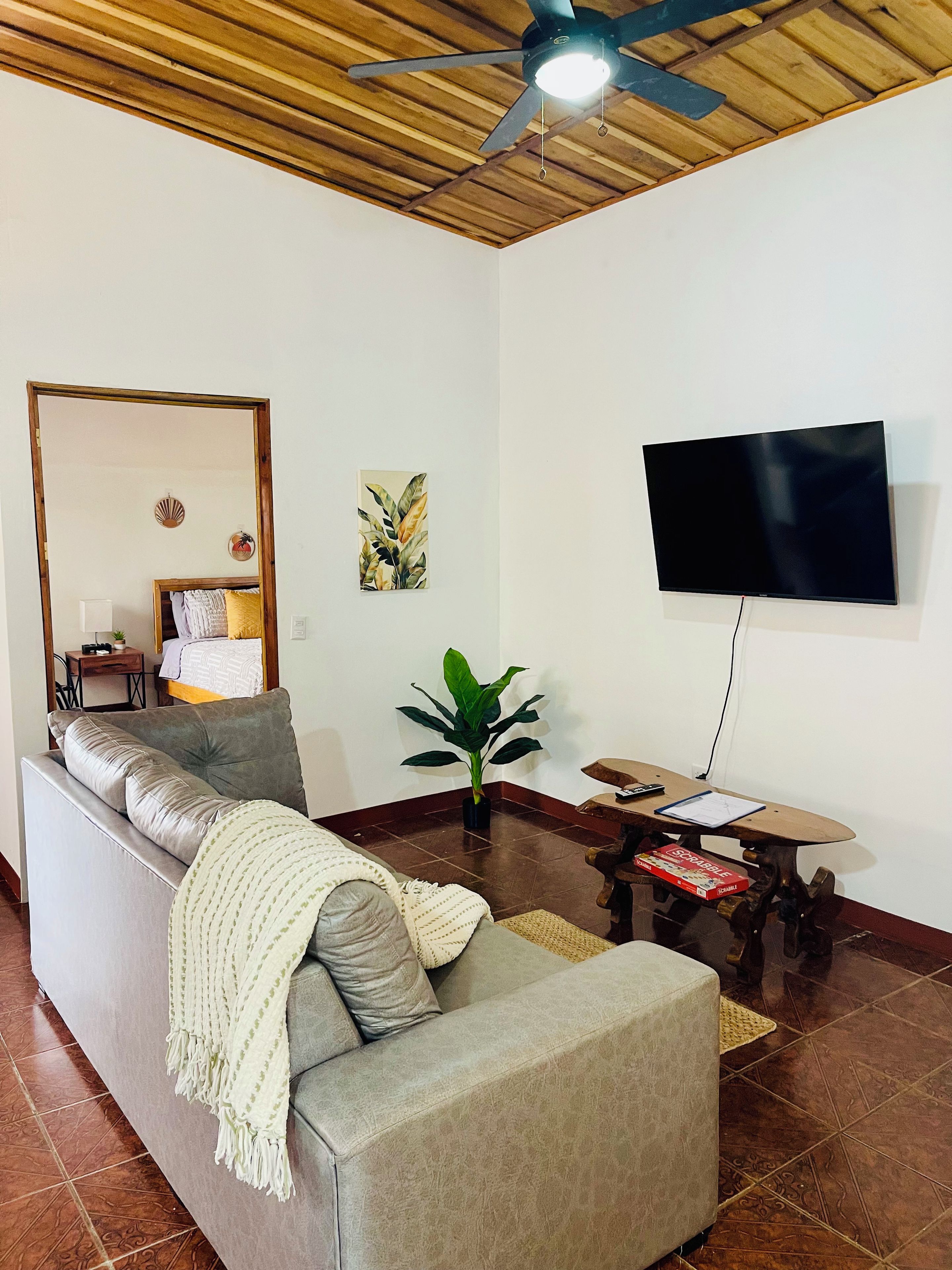 A living room with a sofa, a television, a ceiling fan, a plant, and a small table with a board game.