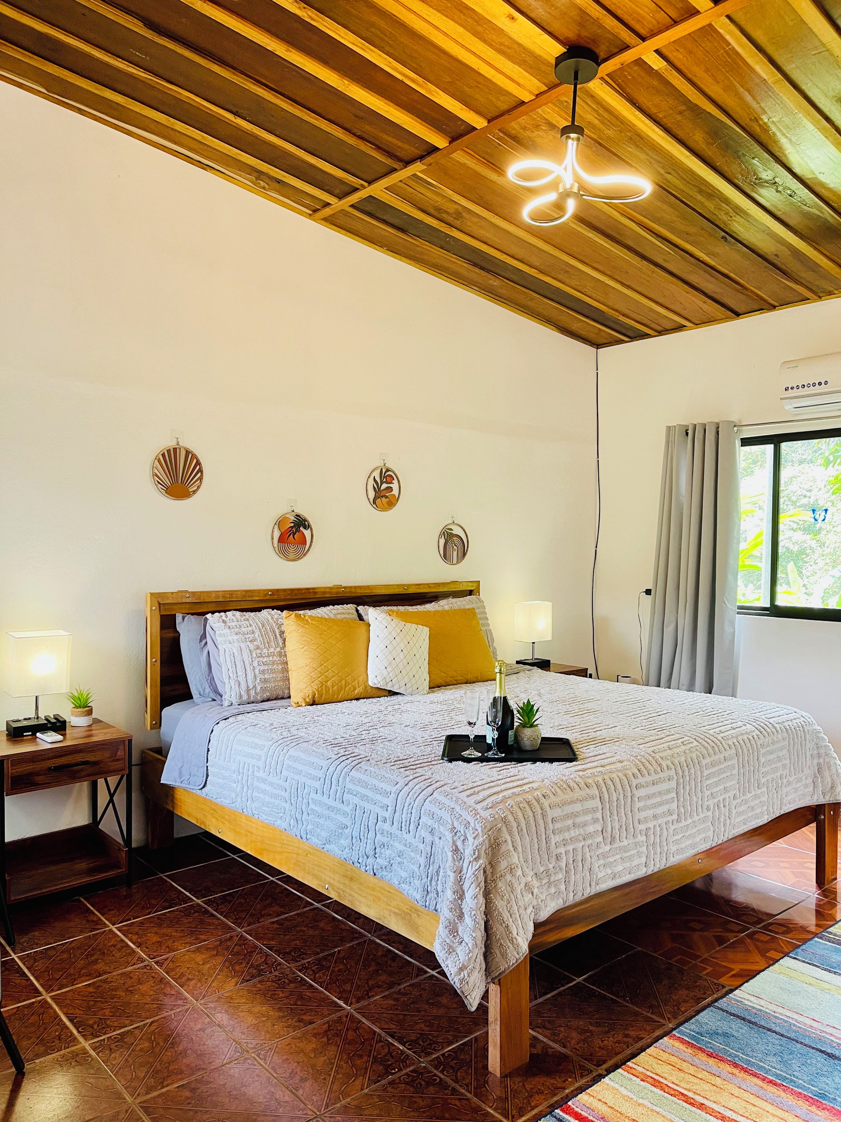 Een slaapkamer met een houten bedframe, een wit beddegoed met structuur en een nachtkastje met een lamp en een kleine plant.