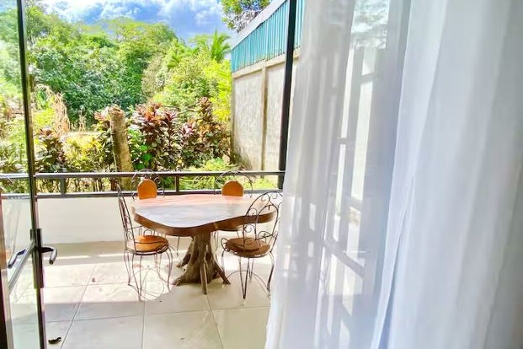 Ein Balkon mit Tisch und Stühlen, Blick ins Grüne und ein Gebäude im Hintergrund.